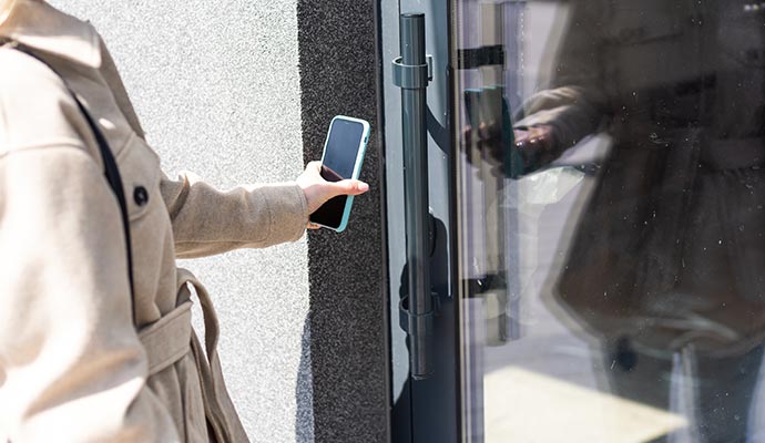 A woman entering through the door while using her cell phone's entering system